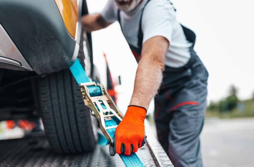 Tow truck operator securing a vehicle with a ratchet strap during roadside towing service.